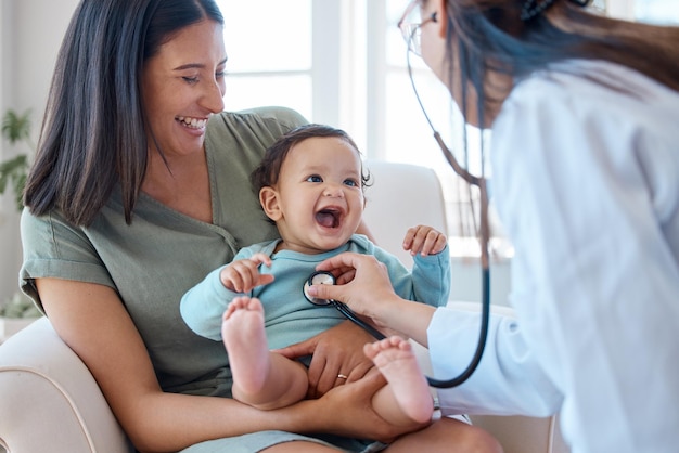 Foto ella sabe cómo poner una sonrisa en tu cara. fotografía de un bebé sentado en el regazo de su madre mientras lo examina un médico.
