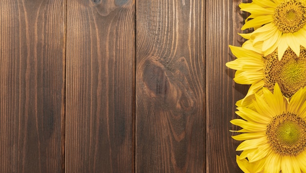 Foto fondo con girasoles sobre una tabla de madera oscura.