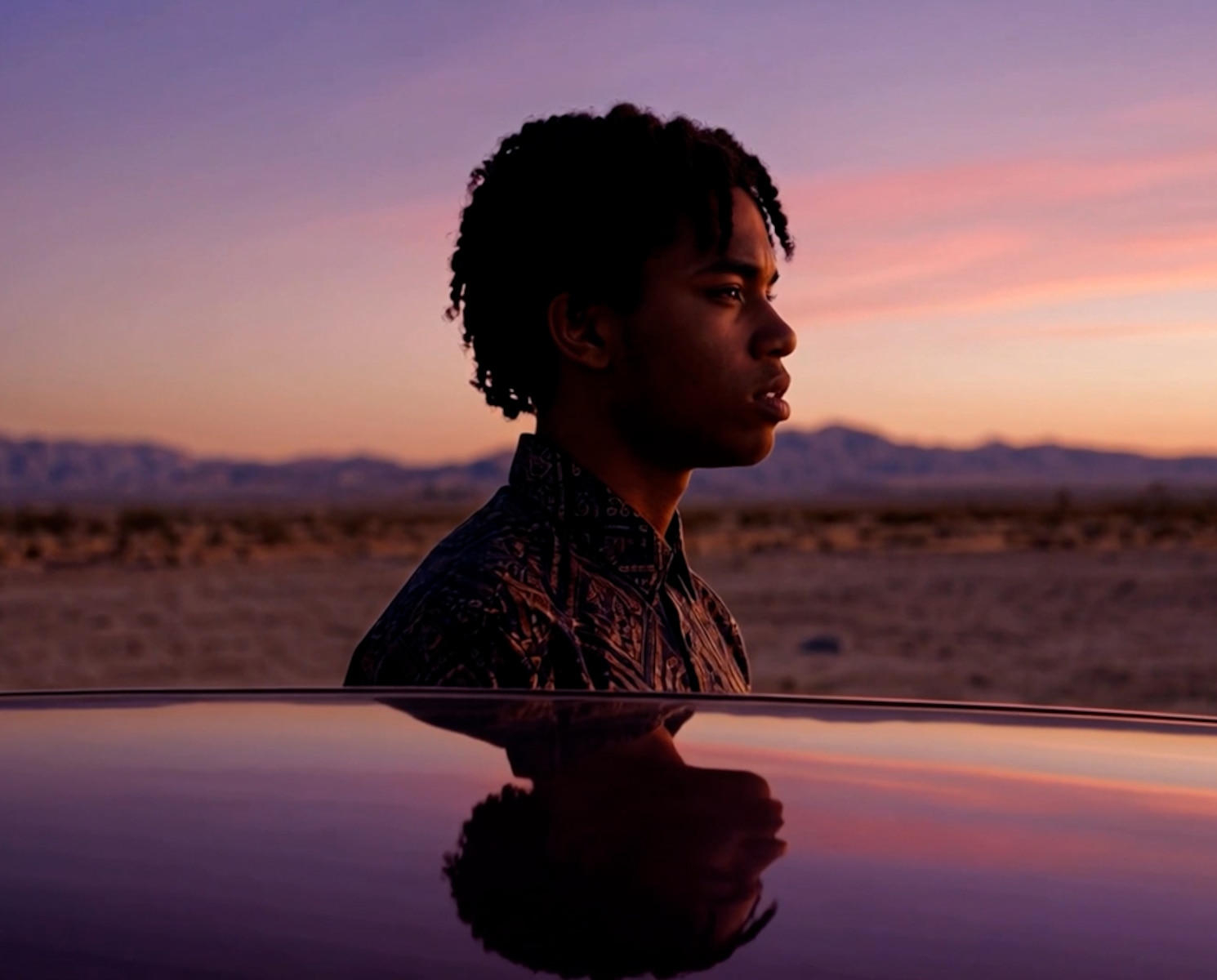 Young man in the desert at dusk, reflected on a car roof