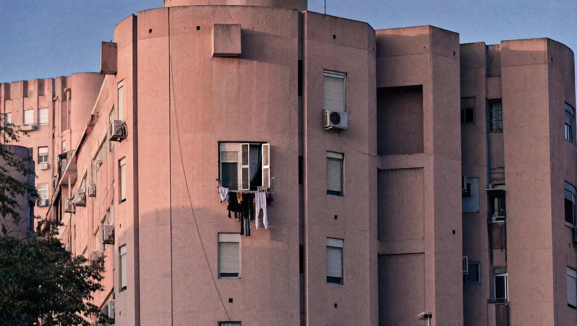 Un edificio brutalista rosa con una ventana abierta y ropa secándose fuera